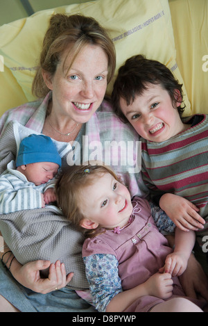 Mother sitting on hospital bed with children and newborn baby, portrait Stock Photo