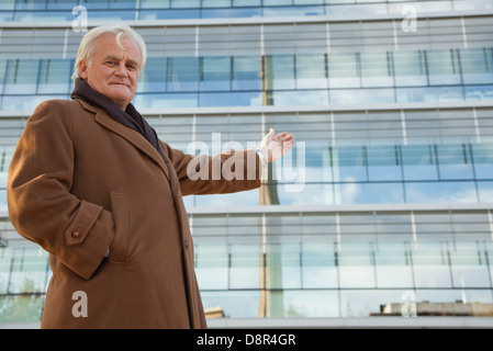 Mature businessman gesturing proudly toward building, portrait Stock Photo