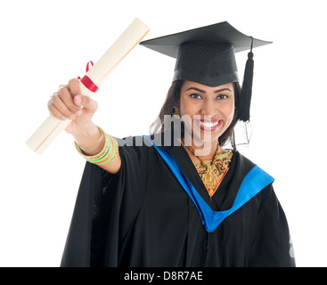 Happy Indian graduate student in graduation gown and cap showing her diploma certificate. Portrait of beautiful Asian female model standing isolated on white background. Stock Photo