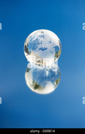 Crystal Glass globe / earth / world on a mirror reflecting blue sky Stock Photo