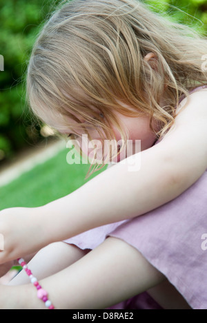 Little girl sitting outdoors, playing with beaded necklace Stock Photo