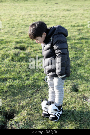 It's a photo of a little child boy who is in a grass field. he looks at something on the ground that catches his attention Stock Photo