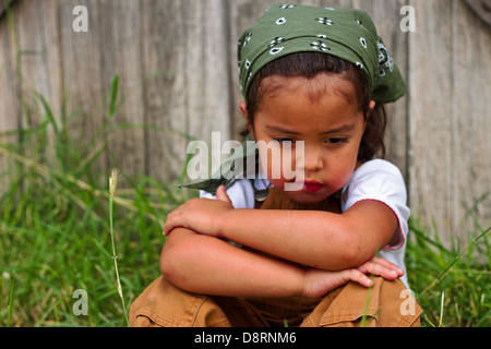 young girl sitting and thinking in front of a wooden barn Stock Photo