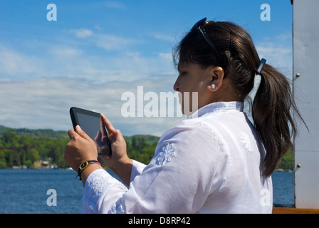 Asian lady on Windermere passenger boat, taking pictures on a tablet computer, Lake District National Park, Cumbria, England UK Stock Photo