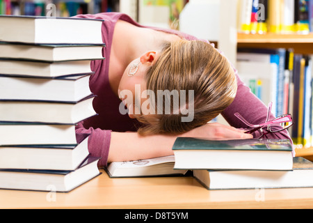 Student - Young woman in library with books learning, she is asleep, tired and overworked Stock Photo