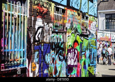 Youngsters in alley spraying colourful graffiti on wall of building in city Stock Photo