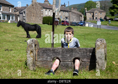 Bainbridge, Richmondshire, North Yorkshire, UK 4th June, 2013. Kevin Harvey, 9 from Redcar in the village stocks,  a member of the travelling community en-route to the Appleby Horse Fair in Cumbria.  The Fair is an annual gathering of Gypsies and Travellers which takes place on the first week in June, and has taken place since the reign of James II, who granted a Royal charter in 1685 allowing a horse fair 'near to the River Eden'. Credit:  Mar Photographics/Alamy Live News Stock Photo