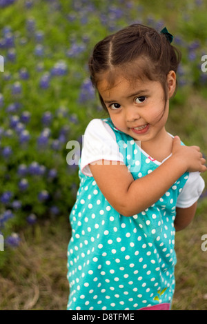 young girl wearing polka dot dress stands beside blue bonnets near Hondo, TX Texas Stock Photo