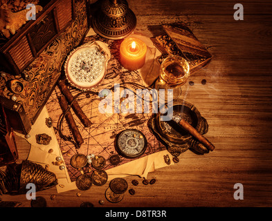 Closeup of pirates booty on wooden table, cigars smoke, glass of wine, map with way to search treasure, stolen antique jewelry Stock Photo
