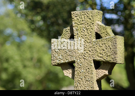 Celtic cross in cemetery with leafy green background. Stock Photo