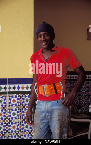 Man wearing red shirt and orange safety harness, window-cleaner, leaning on colourful wall smiling at camera, Havana, Cuba Stock Photo