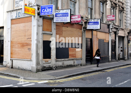 A woman walks past a boarded up shop in central London, UK. Stock Photo