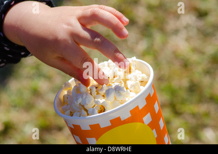 Close-up of child's hand taking popcorn from a cup. Stock Photo