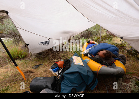 Kayaker sleeping in inflatable kayak under a tarp on a trip down Idaho's Bruneau River. Stock Photo