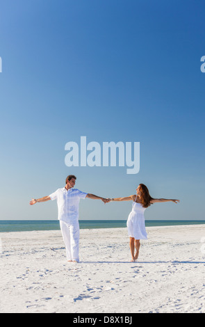 Middle aged happy man and woman romantic couple in white clothes dancing on a deserted tropical beach with bright clear blue sky Stock Photo
