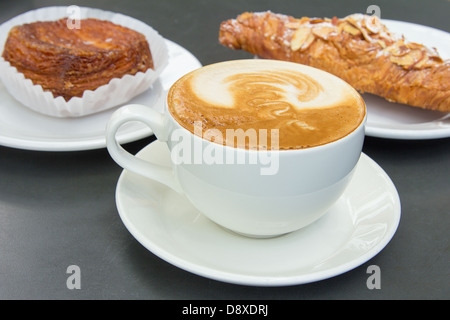 Cup of Caffe Latte with Almond Croissant and Flaky Pastry in Background Stock Photo