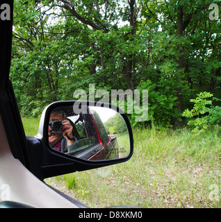 Reflection of a woman who photographs the landscape through the open car window