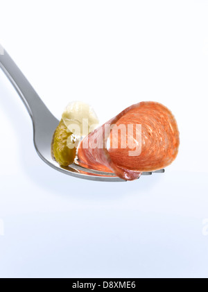 Slice of dried sausage,small onion and gherkin on a fork Stock Photo