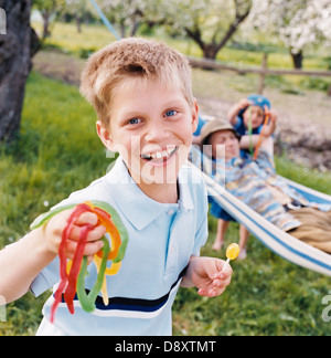 A smiling boy with sweets in the hands and a man lying in a hammock in the background. Stock Photo
