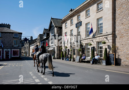 People on horses horse riders riding past village pub and cottages on Main Street Kirkby Lonsdale Cumbria England UK United Kingdom GB Great Britain Stock Photo
