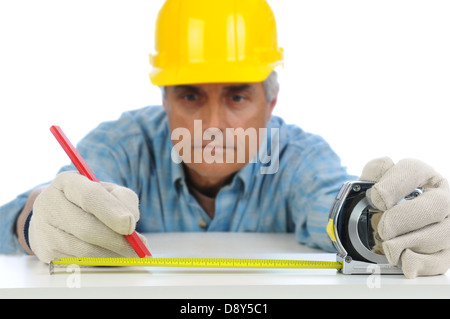 Closeup of a construction worker in hard hat using a measuring tape to mark cut line on a board. Stock Photo