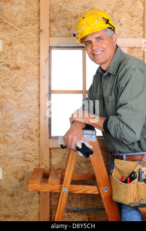 Closeup of a carpenter leaning on a ladder in front of a wall he is building. Vertical Format. Stock Photo