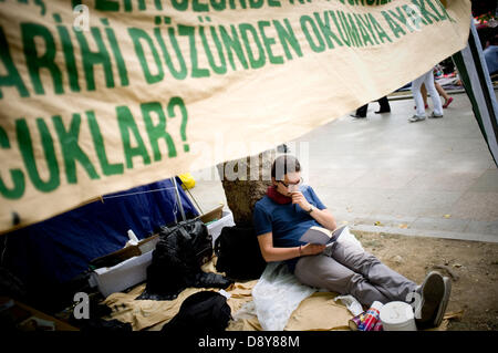 Istanbul, Turkey. 6th June, 2013. A youth reads a below a banner. After several days of conflict, Taksim Square in Istanbul was quiet on 6th June, with people camping out and people chanting slogans against the government. Credit:   Jordi Boixareu/Alamy Live News Stock Photo