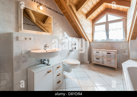 bathroom of a flat in attic with basin, mirror, light, window, toilet, bathtub, cabinets and wooden ceiling Stock Photo