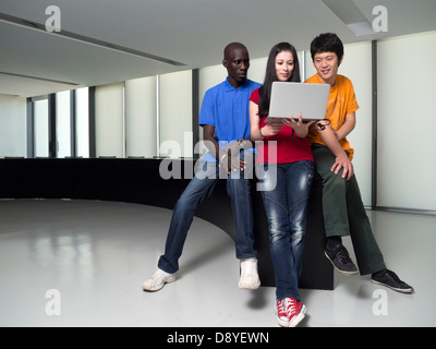 Black man, asian man and caucasian woman gathered around a laptop computer Stock Photo