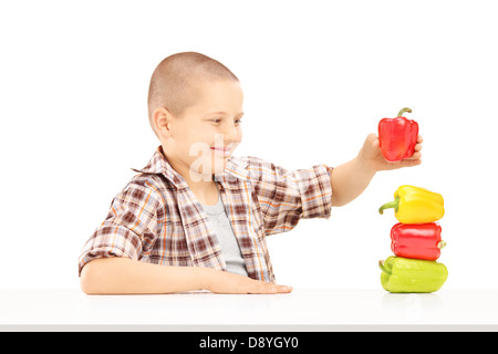 Little smiling boy holding colorful peppers on a table isolated on white background Stock Photo