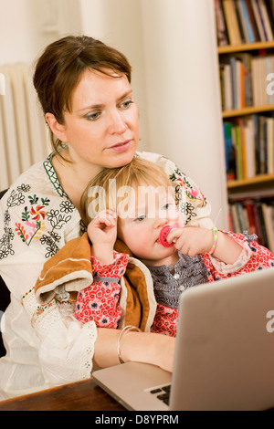 Woman using laptop with daughter on lap Stock Photo