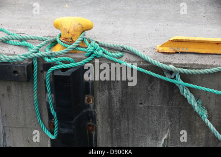 Yellow mooring bollard with green naval rope on the pier Stock Photo