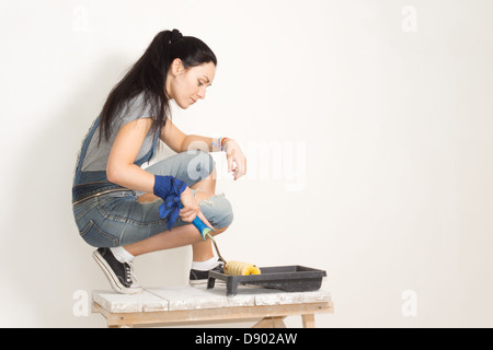 Woman using a roller to paint a wall while renovating or redecorating her house taking paint from a plastic tray Stock Photo