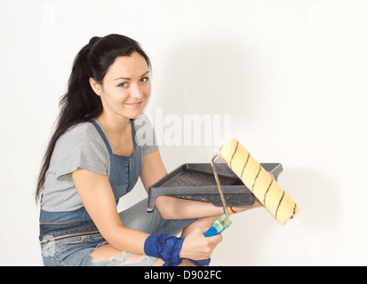 Smiling young woman holding a paint tray and roller in her hands as she prepares to start painting her house Stock Photo