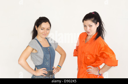 Two capable confident young woman posing in overalls and dungarees with their hands on their hips Stock Photo