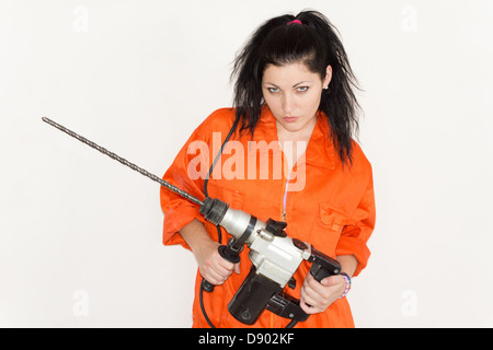 Woman with an attitude standing glowering up at the camera with a large cordless drill with a long masonry bit in her hands Stock Photo