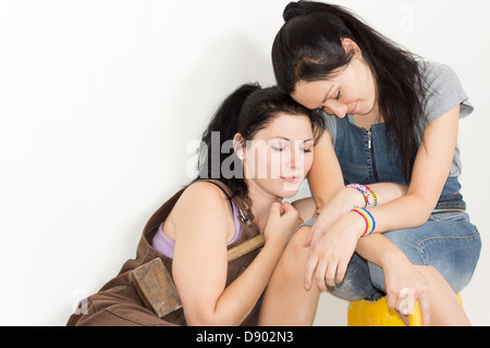 Two affectionate sisters resting with their arms entwined and heads touching as they take a break from a renovation project Stock Photo