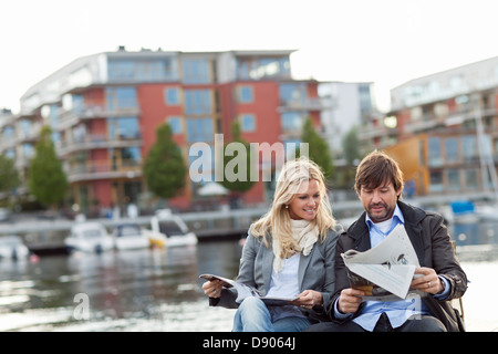 Couple sitting by water and reading newspaper Stock Photo