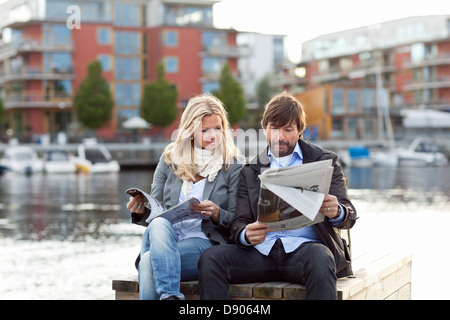 Couple sitting by water and reading newspaper Stock Photo