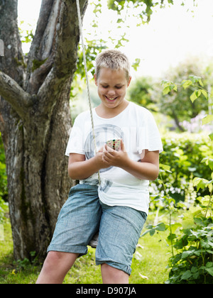 Teenage boy swinging on rope swing and text messaging Stock Photo