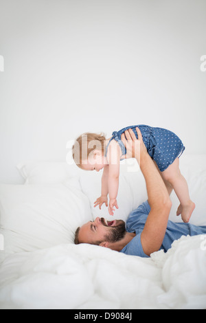 Man lying on bed and holding little daughter Stock Photo