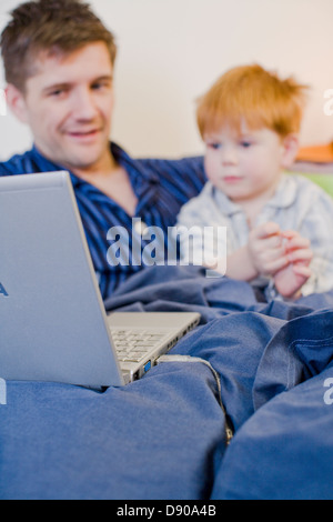 A father and son using a laptop in bed, Sweden. Stock Photo