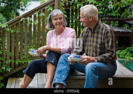 Senior couple sitting on steps, having coffee Stock Photo