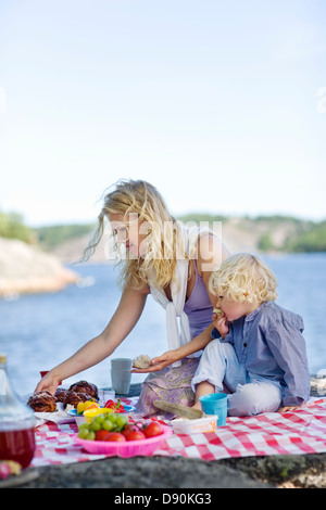 Mother and son on picnic blanket with food beside lake Stock Photo