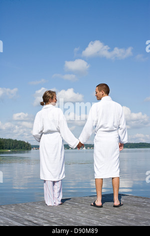 Young couple in bathrobe standing on jetty, holding hands Stock Photo