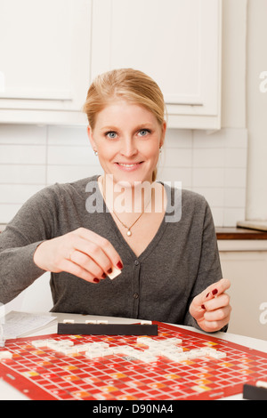 Portrait of young woman playing board game in kitchen Stock Photo