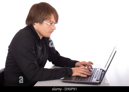 Concentrated young man with black shirt working seriously on a laptop. Isolated on white background. Stock Photo