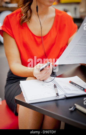 Young woman reading documents and talking on mobile phone using earbud Stock Photo