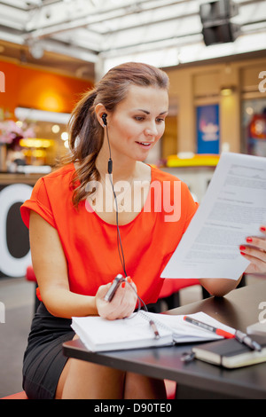 Young woman reading documents and talking on mobile phone using earbud Stock Photo
