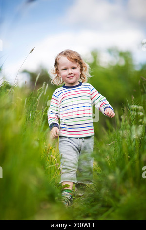 Boy walking through long grass in field Stock Photo